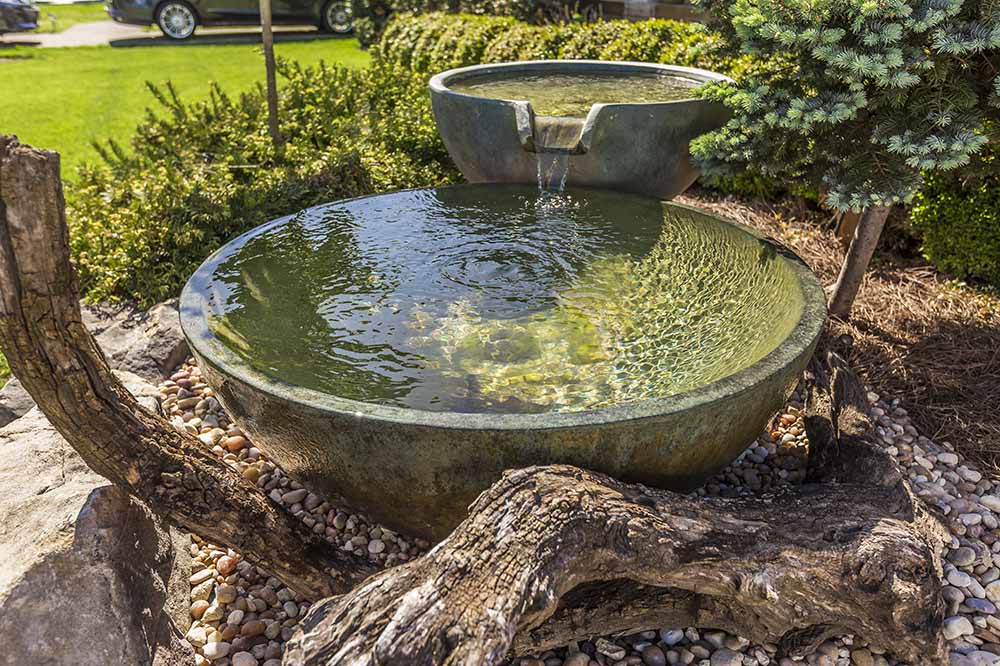 Modern spillway bowls pouring into a pebbled basin.