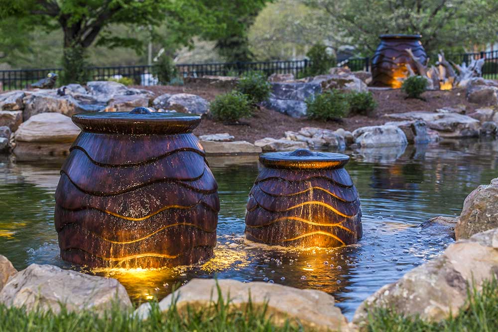 Lit urn fountains inside a JVI koi pond at dusk