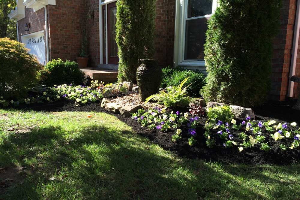 A single vase fountain set into a planted front-yard bed.
